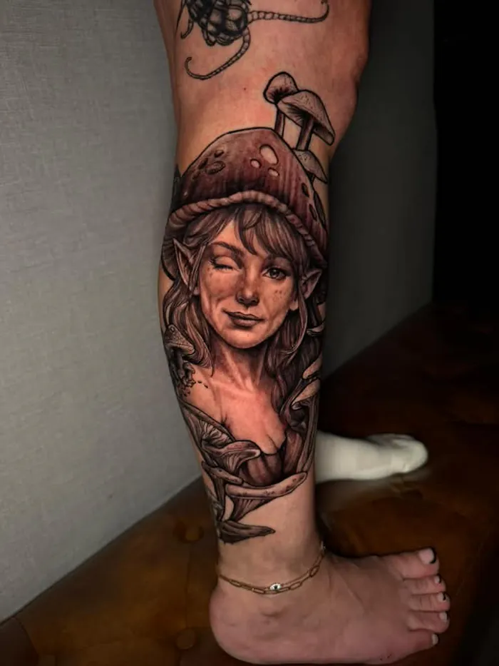 Black and grey realism calf tattoo of a fairy portrait with a mushroom hat by Duk Tattoo, Boca Raton, Florida
