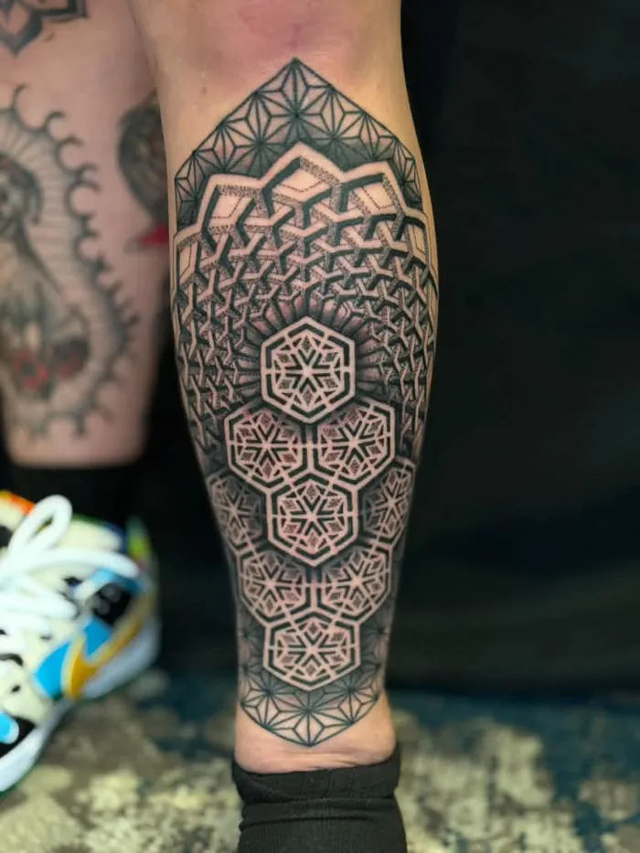 Calf sacred geometry tattoo with hexagons, flower of life and dotwork gradients in black and grey by Duk Tattoo, Florida
