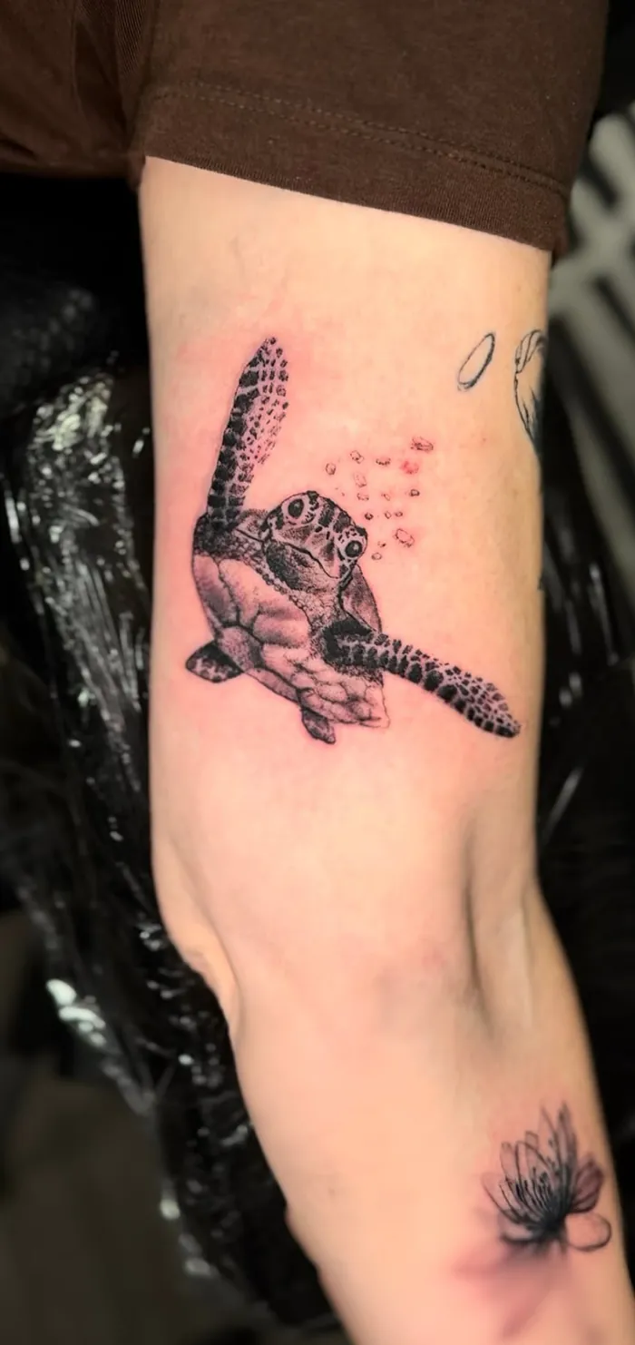 Fine line forearm tattoo of a sea turtle with small pink accents by Duk Tattoo, Boca Raton, Florida