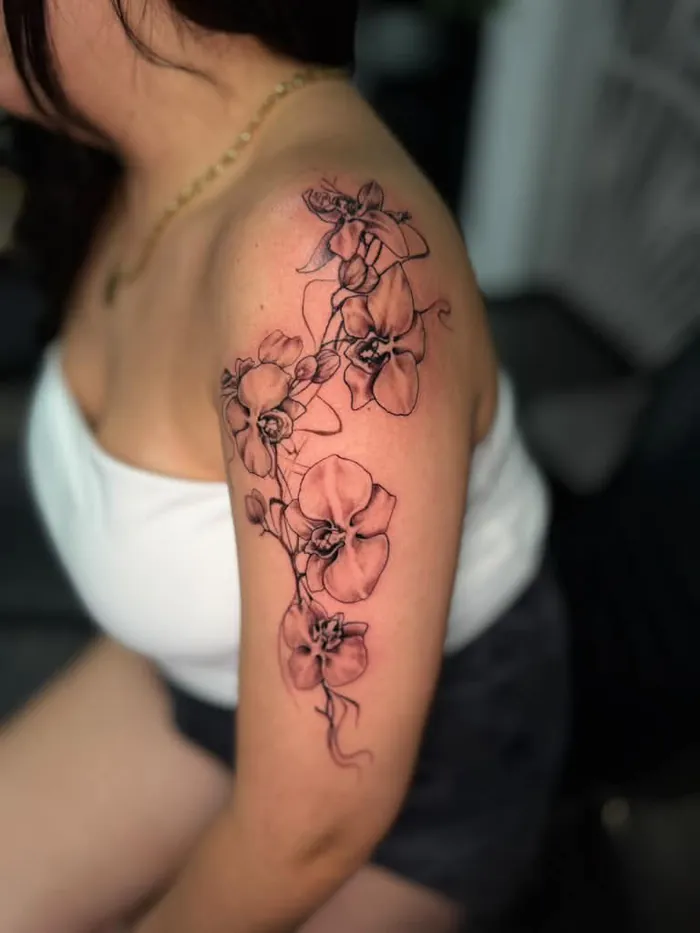Fine line orchid flowers tattoo with soft color on the shoulder and arm of a woman by Duk Tattoo, Boca Raton, Florida