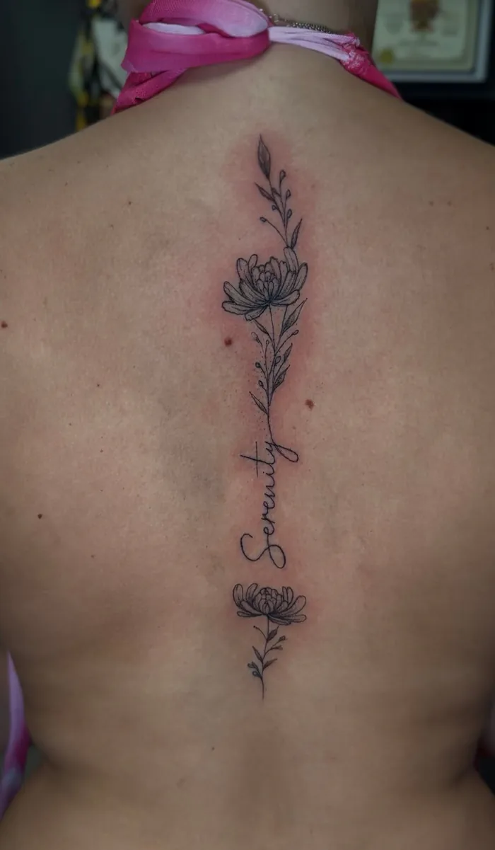 Fine line spine tattoo with flowers and the word Serenity in script on a woman by Duk Tattoo, Boca Raton, Florida
