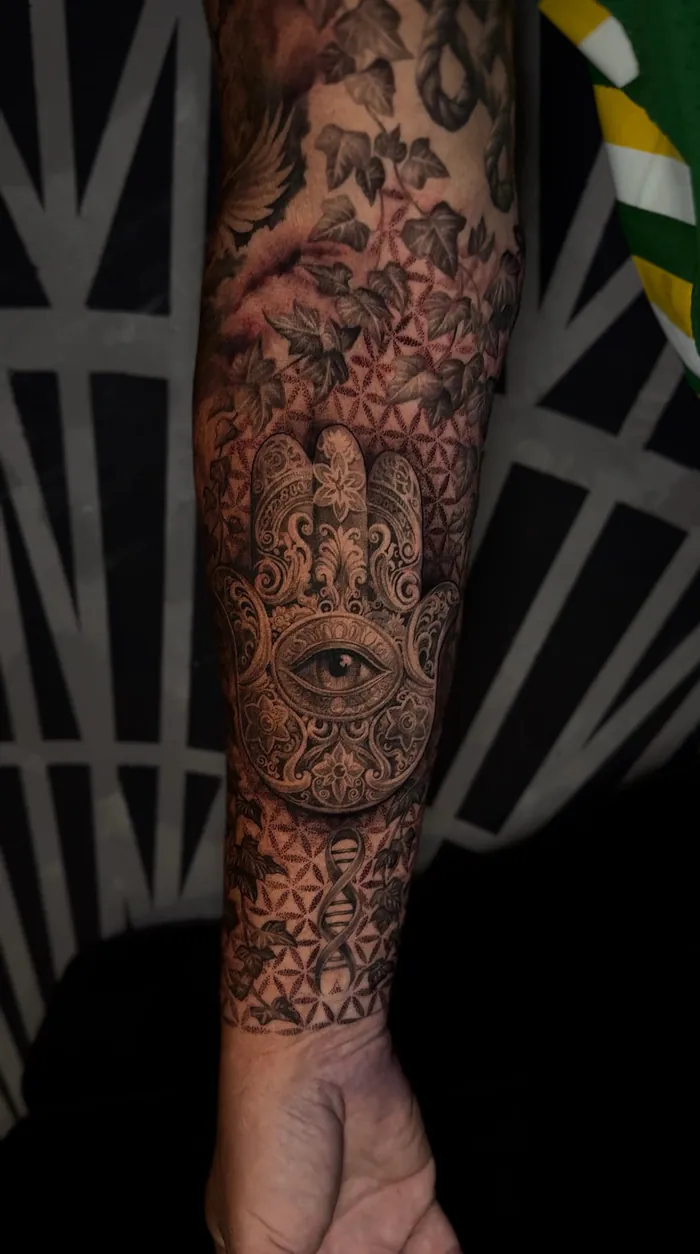 Geometric forearm tattoo of a hamsa hand with an eye, roses and flower of life in black and grey by Duk Tattoo, Boca Raton, Florida