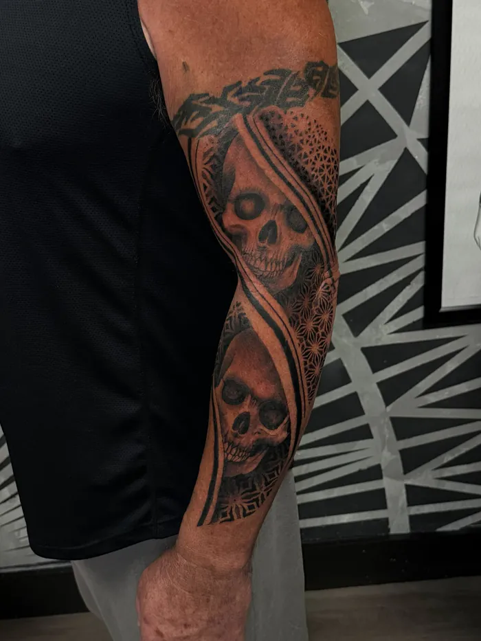 Black and grey forearm sleeve tattoo with skulls and ornamental geometric patterns by Duk Tattoo, Boca Raton, Florida